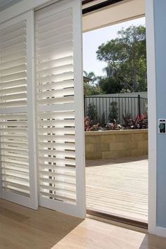 an open door with white shutters and wood flooring in front of a patio