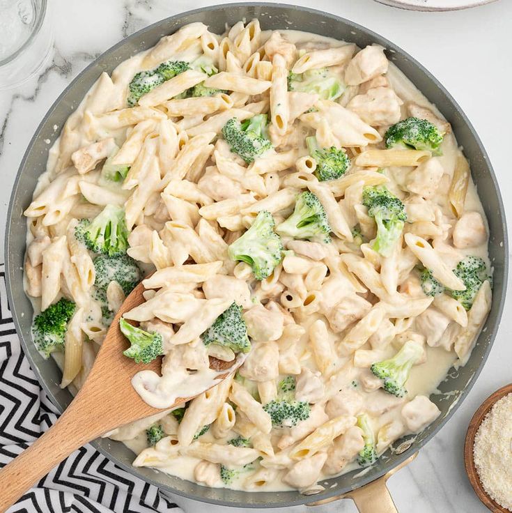 a skillet filled with pasta and broccoli on top of a marble counter