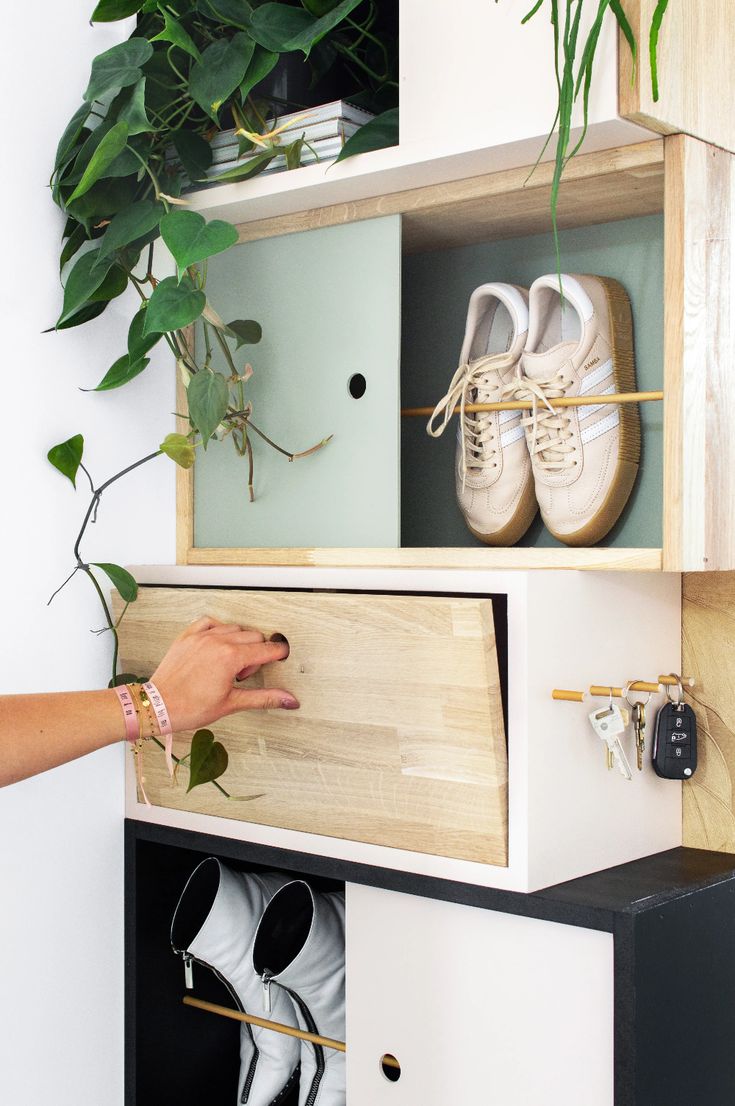 a person's hand reaching into a shoe rack with shoes on it and plants in the background