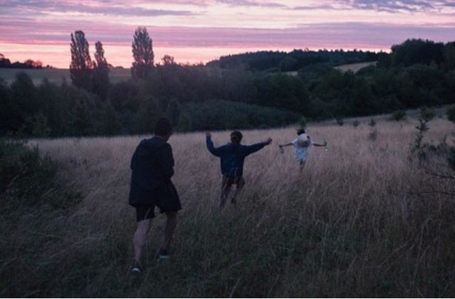 three people standing in a field with their arms up and one person pointing at the sky