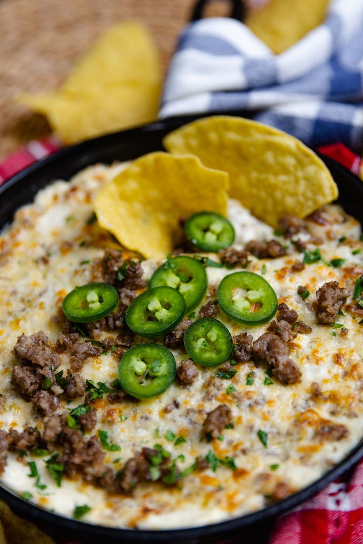 a black bowl filled with cheese and jalapenos next to tortilla chips