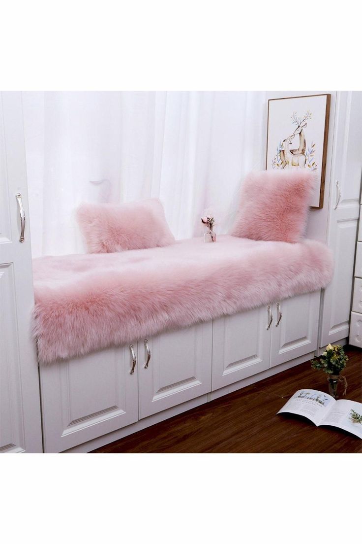 a pink bench with two pillows on it in front of a white cabinet and window