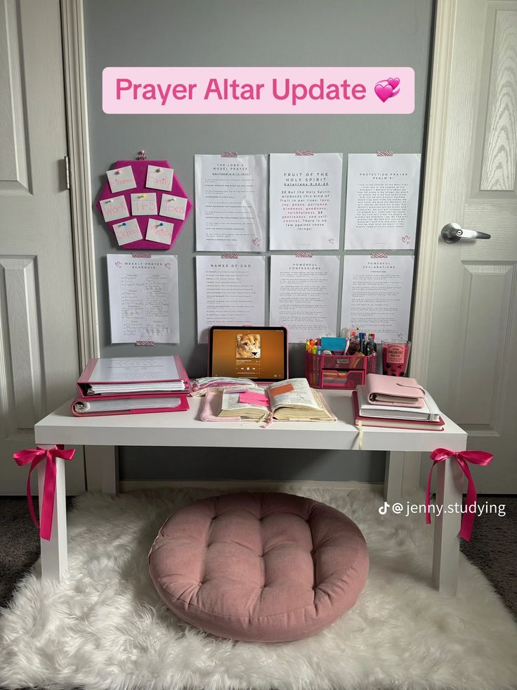 a white desk topped with lots of books and pink accents next to a wall mounted sign that says prayer altar update