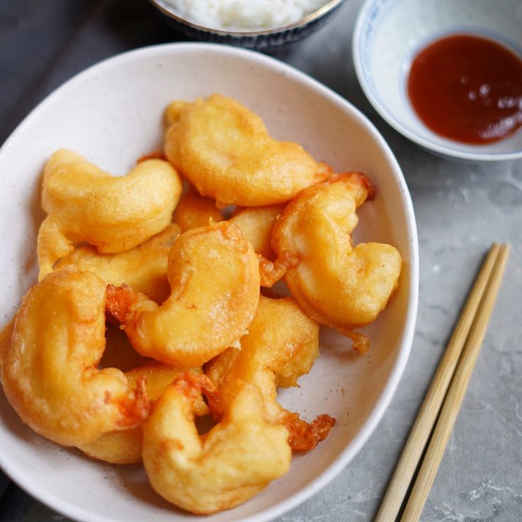 a bowl filled with fried food next to chopsticks and sauce on a table