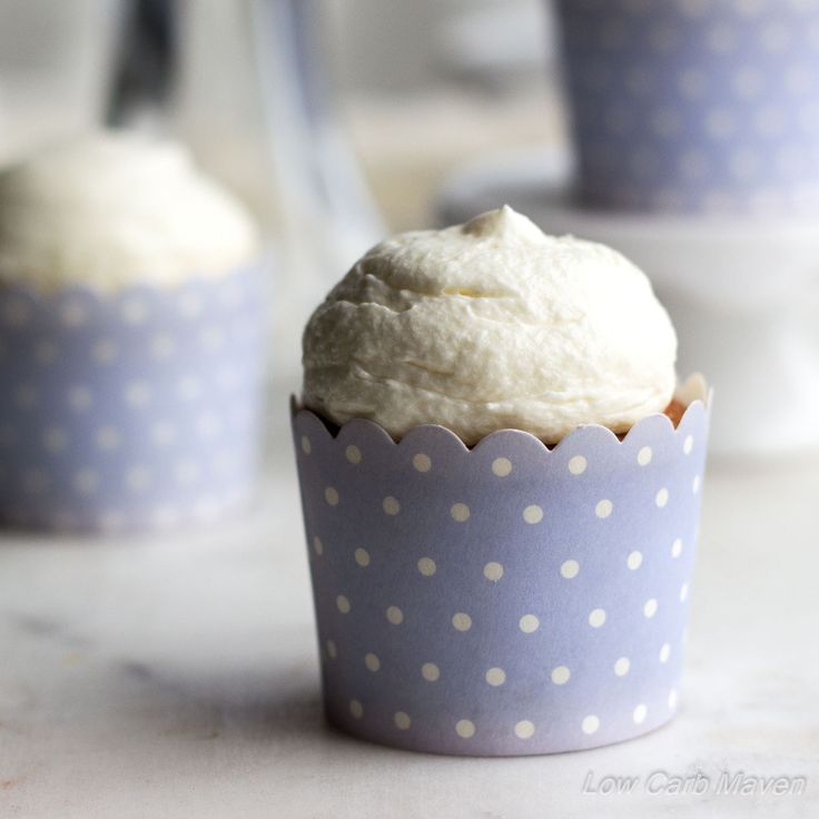 three cupcakes with white frosting and polka dot paper cups in the background