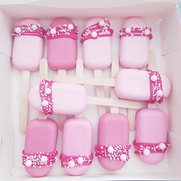 a box filled with lots of pink and white frosted pops next to each other