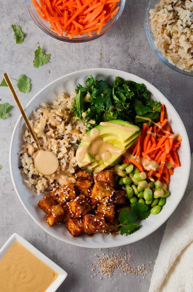 a white bowl filled with rice, carrots and other vegetables next to some dipping sauce