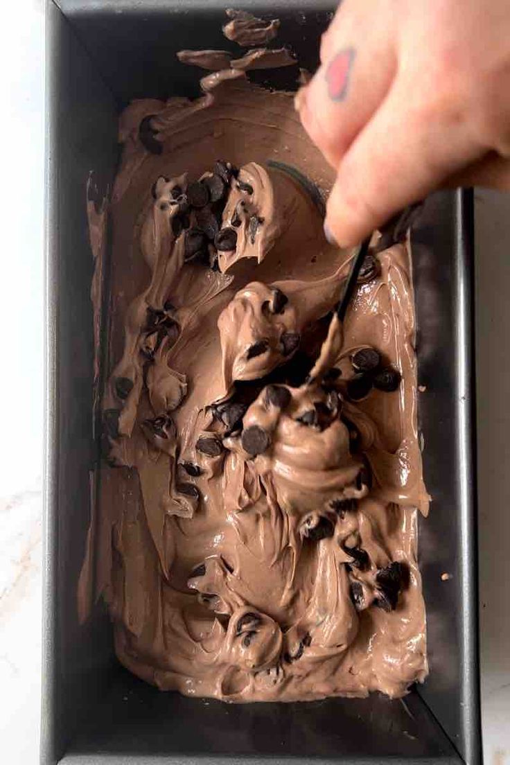 someone is spreading chocolate frosting on top of the cake in a black square pan