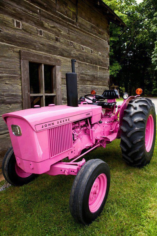 an old pink tractor parked in front of a wooden building with grass on the ground