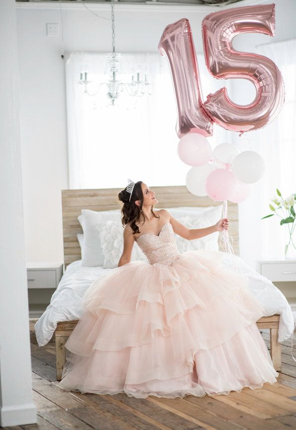 a woman sitting on a bed with balloons in front of her and the number fifteen