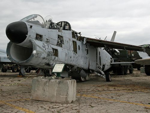 an old fighter jet sitting on top of a cement block next to other planes in the background