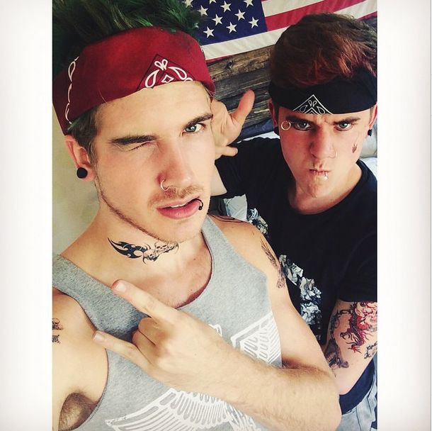 two young men with tattoos and piercings posing for a photo in front of an american flag