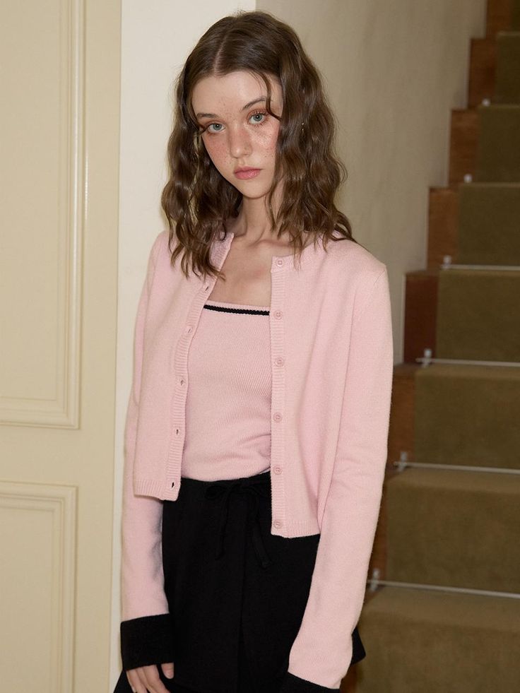 a woman standing in front of stairs wearing a pink cardigan and black pants with her hands on her hips