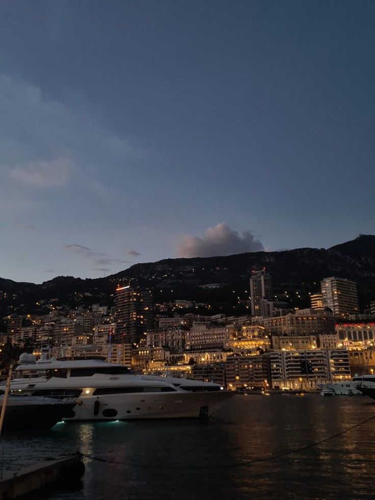 several boats are docked in the water at night near a city with lights on it