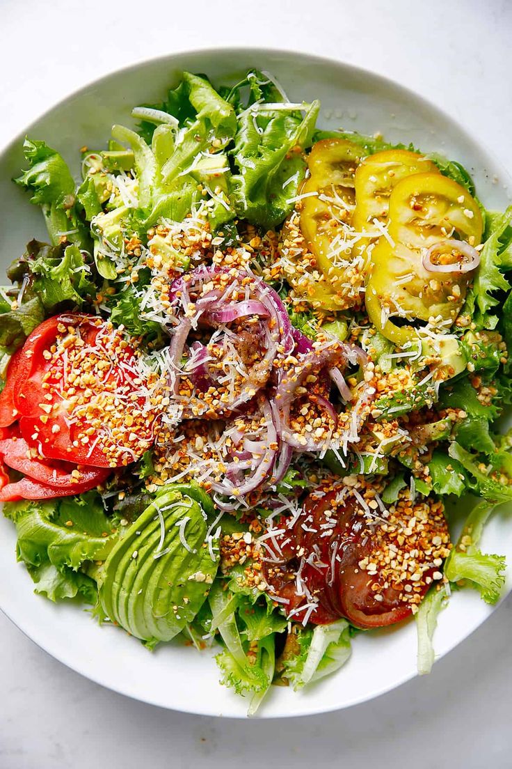 a salad with tomatoes, lettuce and other toppings on a white plate