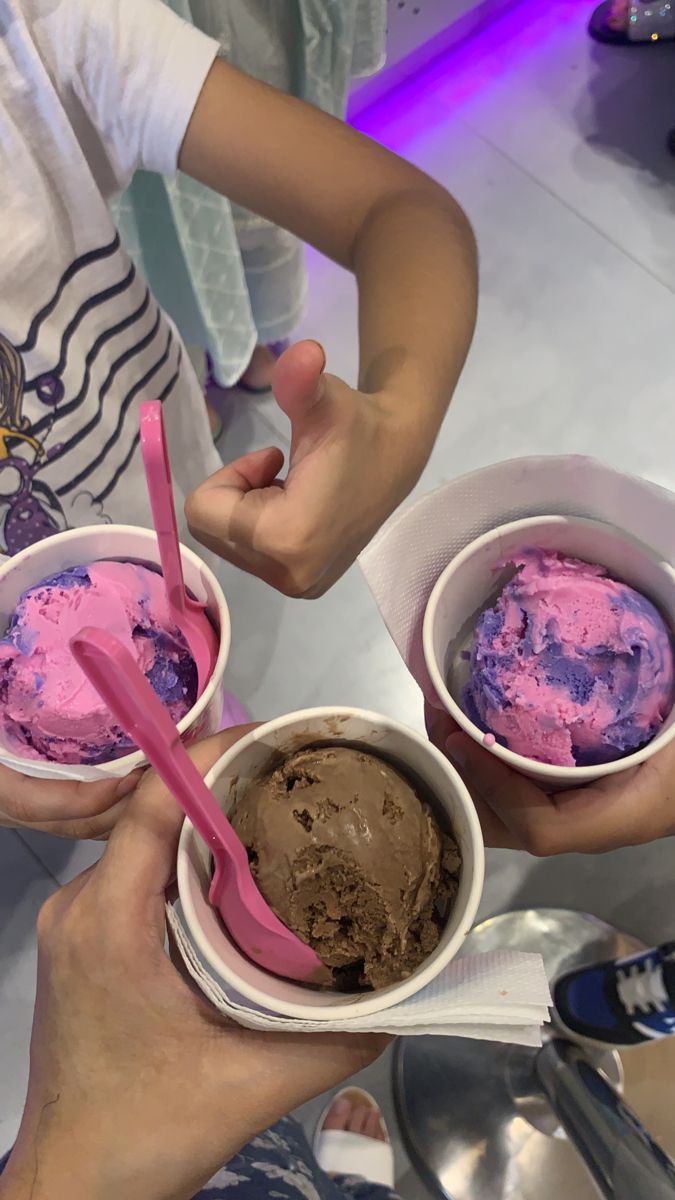 two people holding ice creams in their hands with pink and blue toppings on them