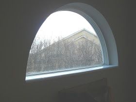 an arched window in the corner of a room with a view of trees outside it