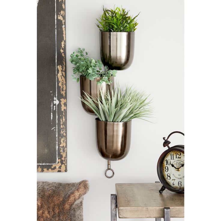 three metal planters are hanging on the wall next to an old clock and table