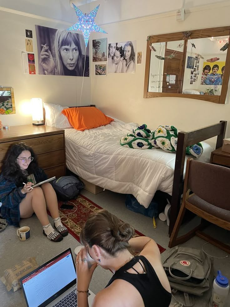 two women sitting on the floor in front of a bed with an open laptop computer