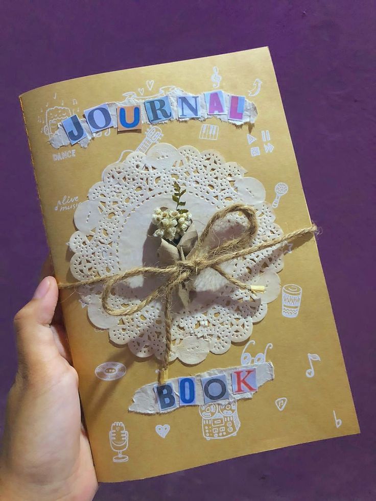 a hand holding an open book with doily on it and writing journal written in blue