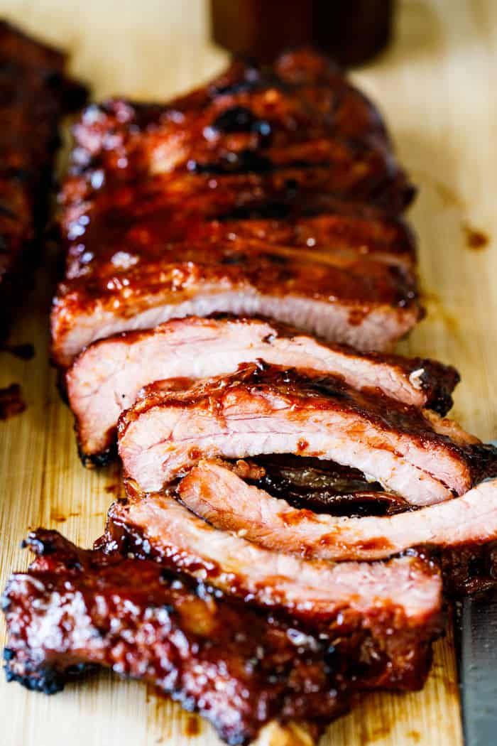 sliced up barbecue ribs on a cutting board with ketchup