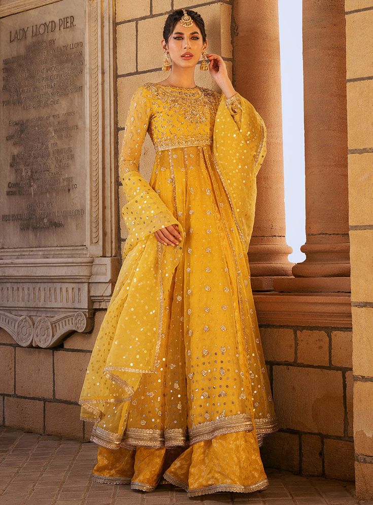 Safeeneh Anarkali Sharara With Dabka Work And Traditional Drape, Anarkali Sharara With Dabka Work, Anarkali Chanderi Sharara With Dabka Work, Eid Anarkali Sharara With Mirror Work, Gold Chanderi Palazzo Set With Sheer Dupatta, Chanderi Sharara With Dabka Work, Gold Floor-length Anarkali Set With Sheer Dupatta, Eid Anarkali Sharara With Sheer Dupatta, Yellow Anarkali Palazzo Set For Eid