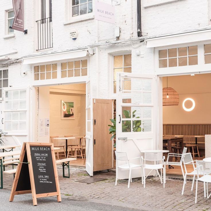 the outside of a restaurant with white chairs and tables in front of it on a cobblestone street