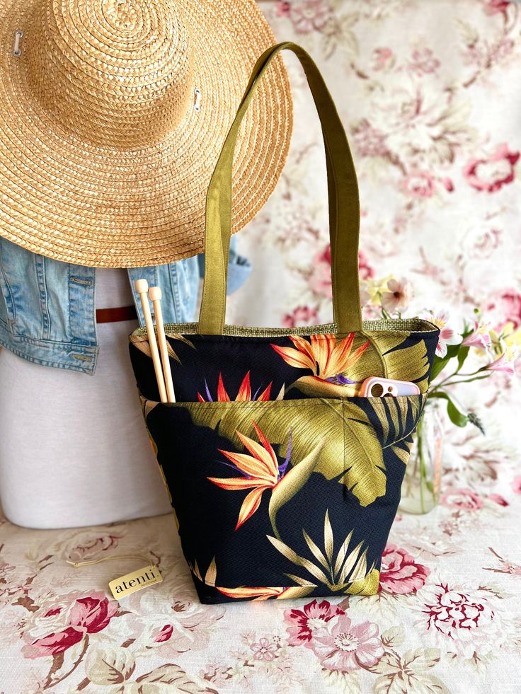 a straw hat is sitting on top of a floral print bag and next to a pair of straw hats