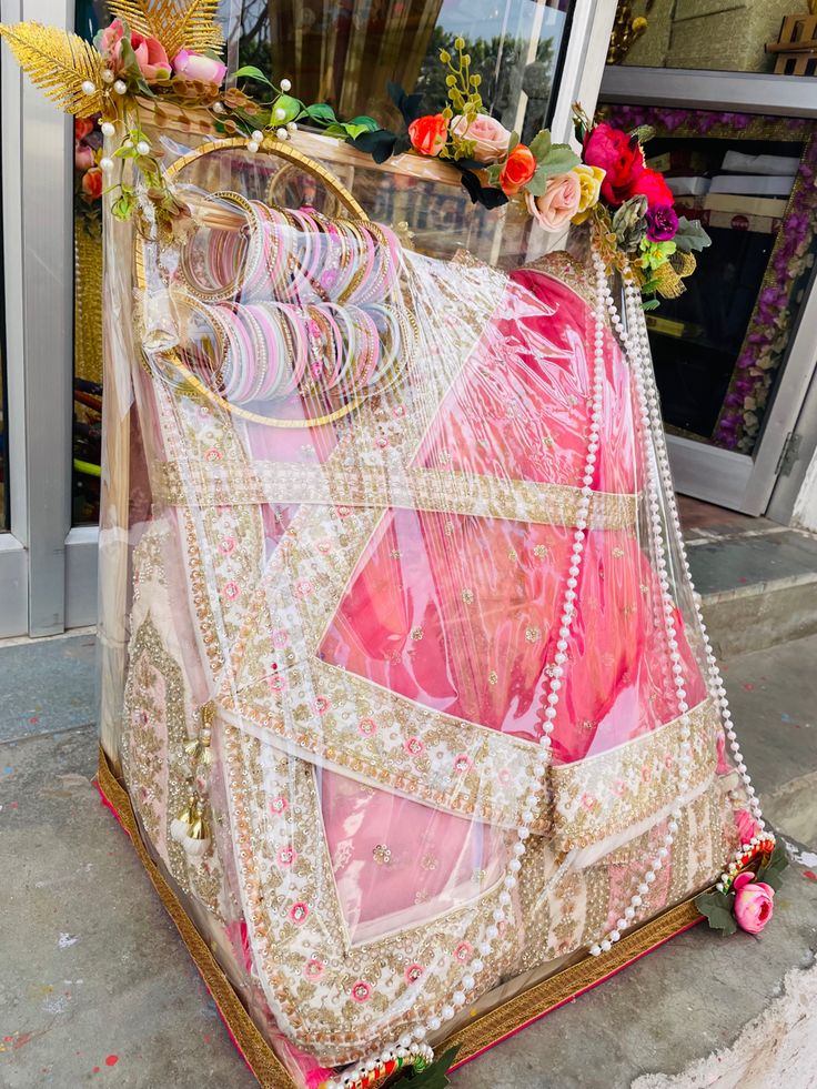 a pink and white sari with flowers on the top is sitting in front of a store