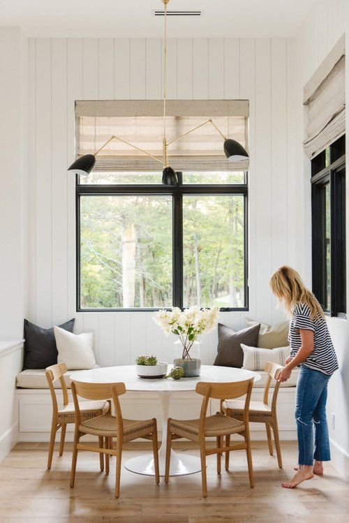 a woman standing in front of a white dining room table with four chairs and a bench