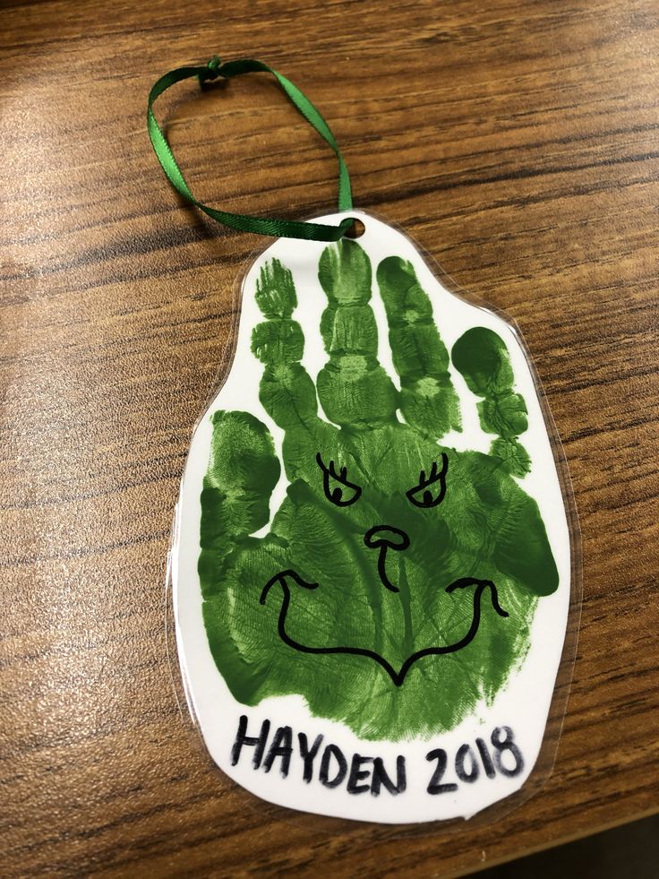 a handprinted ornament on a wooden table with green ribbon hanging from it