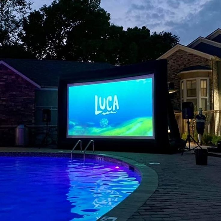 a large projection screen next to a swimming pool at night with the word lucas projected on it