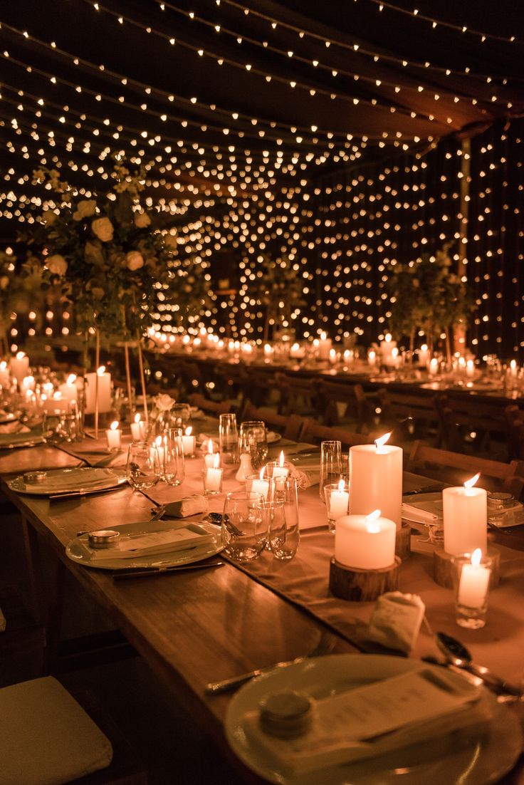 a long table is set with candles and place settings in front of a wall of lights