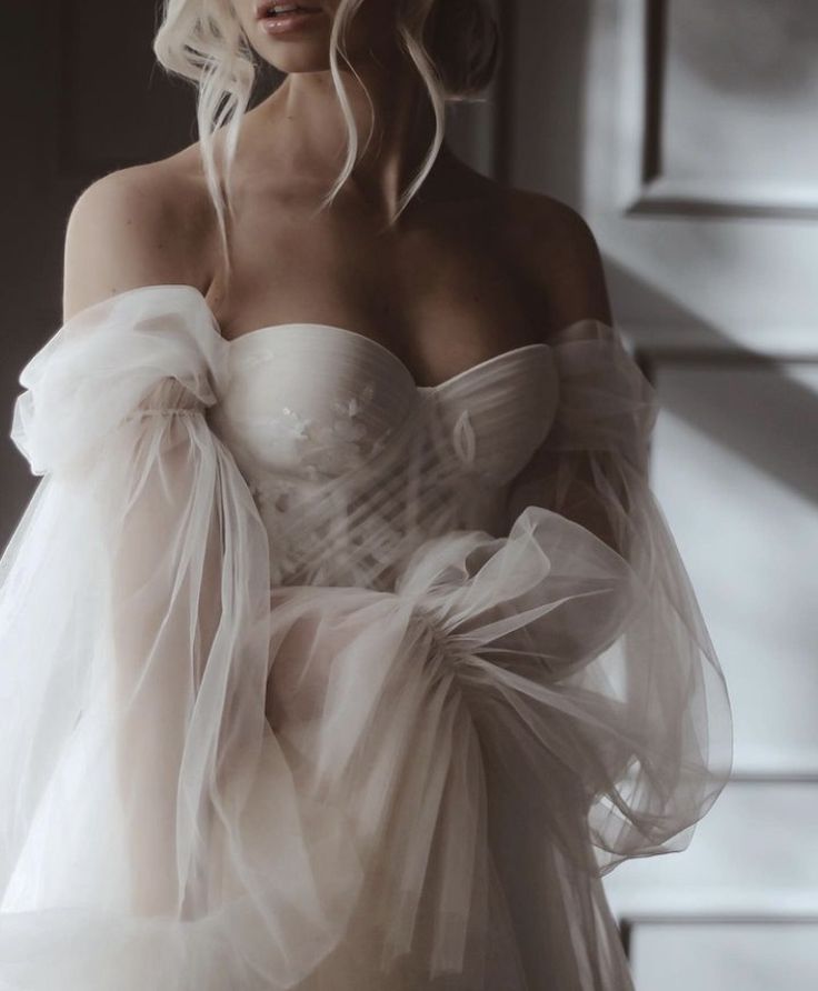 a woman in a white dress with long sleeves and tulle on her arms, posing for the camera