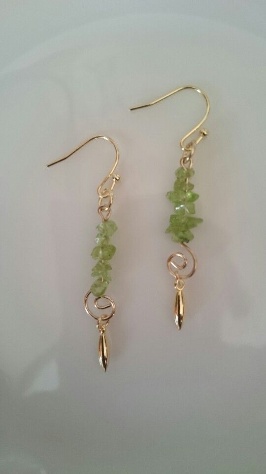 two pairs of gold earrings with green beads and leaves on the end, sitting on a white surface