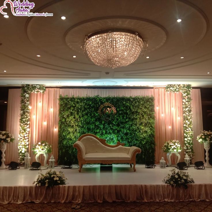 a stage set up for a wedding with flowers and greenery on the wall behind it