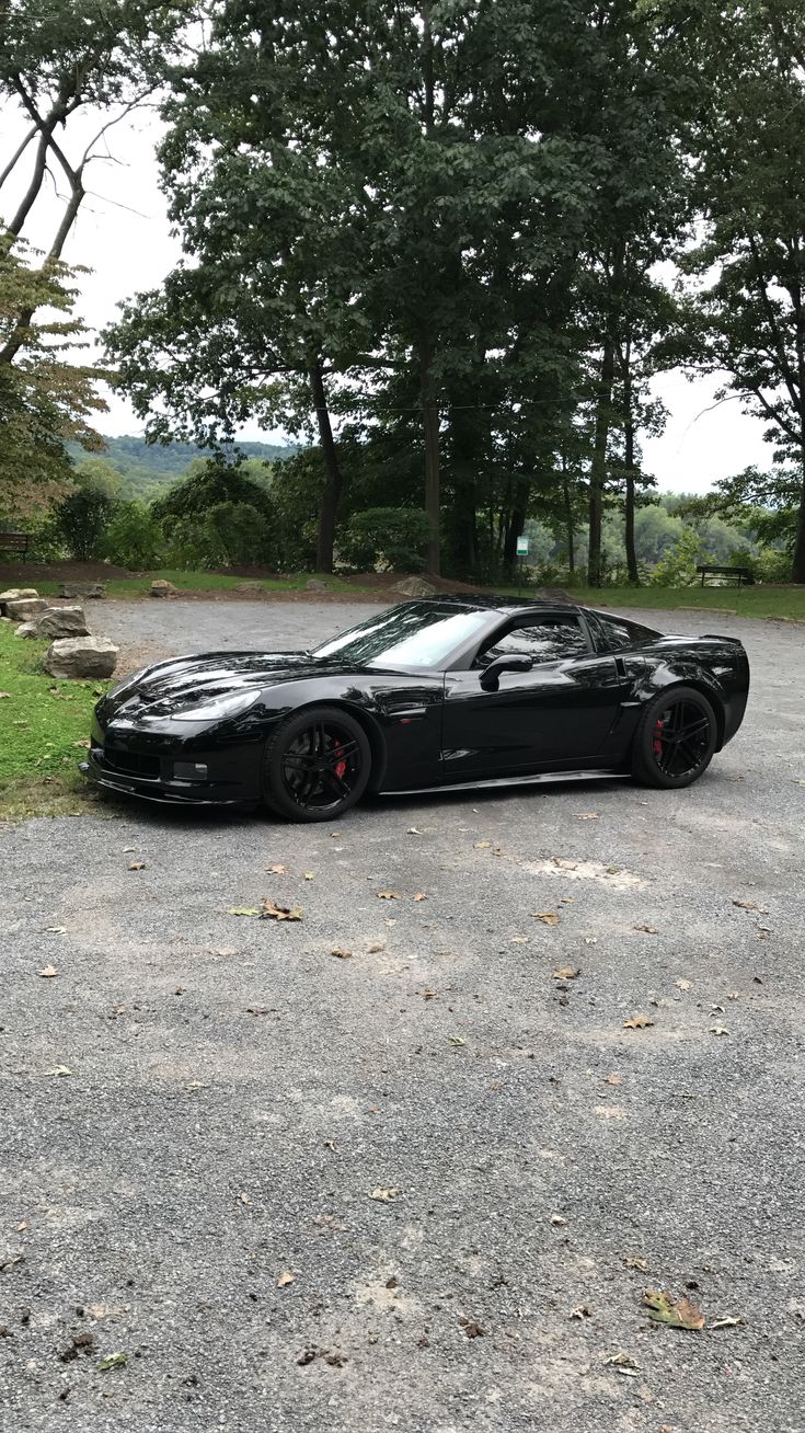 a black sports car parked in the middle of a parking lot next to some trees