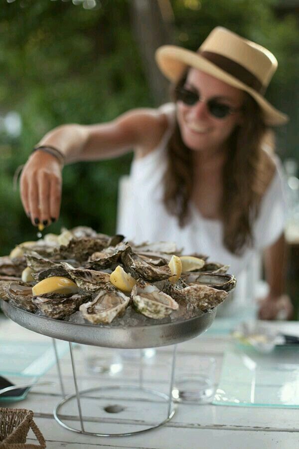 a woman in a hat and sunglasses is serving oysters on a platter with lemon wedges