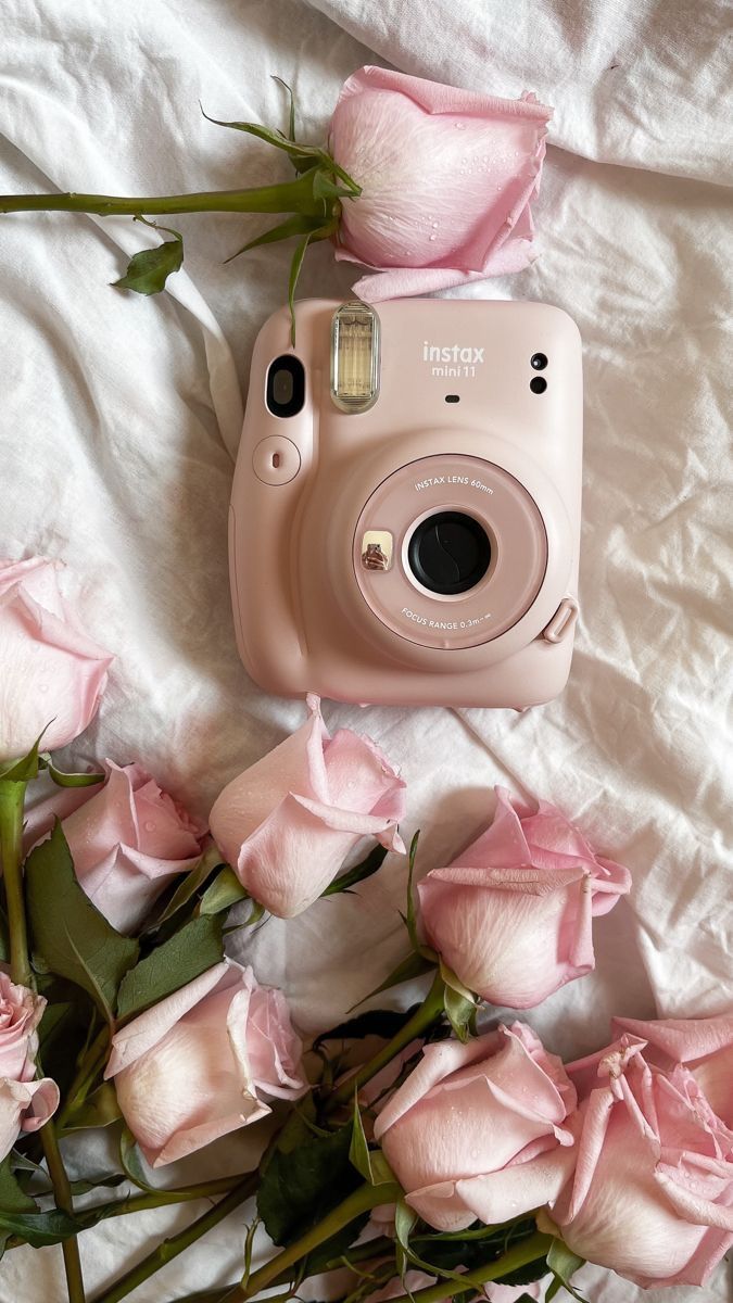 a pink polaroid camera sitting on top of a white sheet next to some pink roses