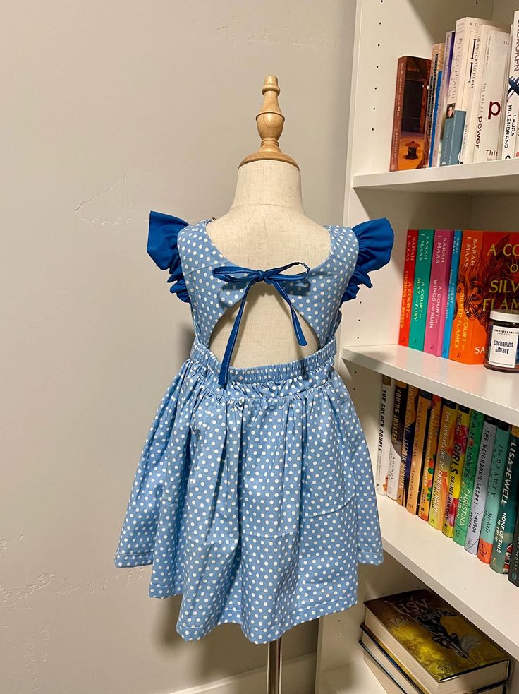 Pictured size 3T This dress features a chargming blue poka dot pattern, flutter sleeves, and an open-back desgin with a bow tie detail. Perfect for any special occasion or everday wear. This dress was crafted by using Peony Patterns Fitted Flutter Sleeve Twirl Dress For Dress-up, Blue Dress With Tie Back And Ruffled Straps, Fitted Twirl Dress With Flutter Sleeves For Dress-up, Blue Flutter Sleeve Dress With Smocked Back, Blue Dress With Smocked Back And Flutter Sleeves, Blue Ruffled Twirl Dress For Dress-up, Blue Flutter Sleeve Dresses For Dress-up, Blue Twirl Dress With Ruffles For Dress-up, Cute Fitted Blue Twirl Dress