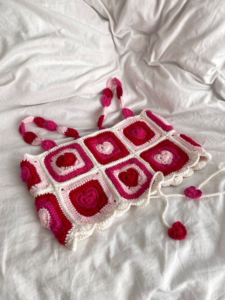 a crocheted purse sitting on top of a white bed next to a pillow