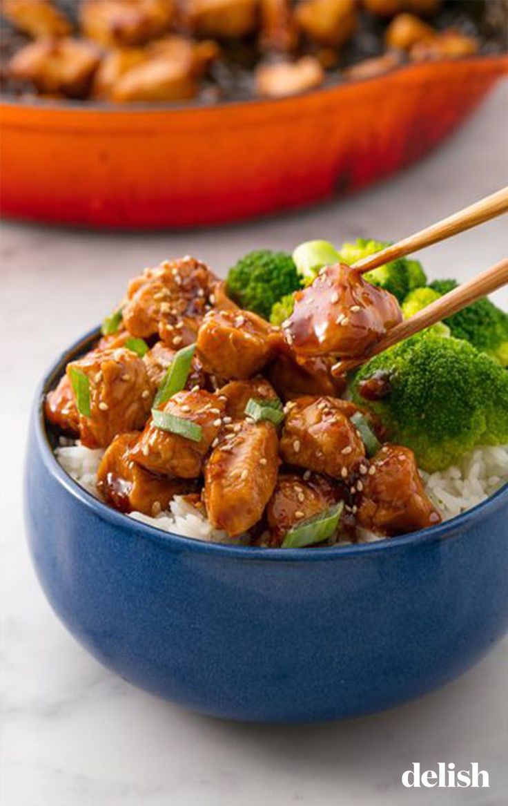 a blue bowl filled with chicken and broccoli on top of white rice next to an orange pan