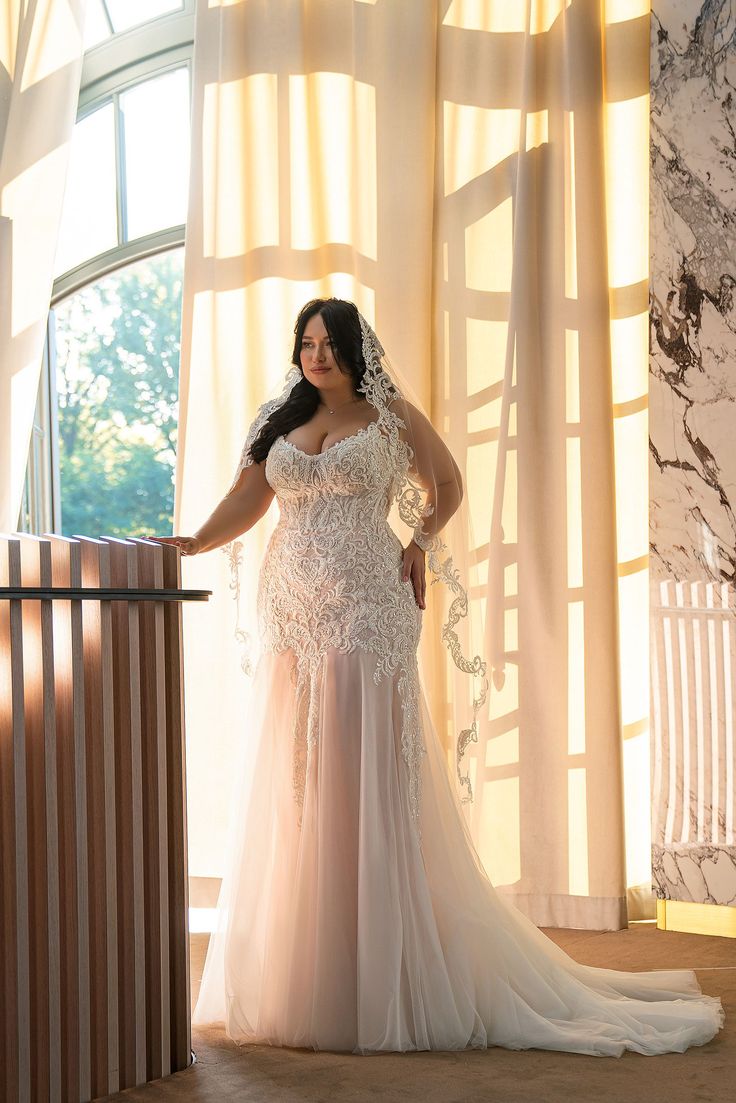 a woman standing in front of a window wearing a wedding dress