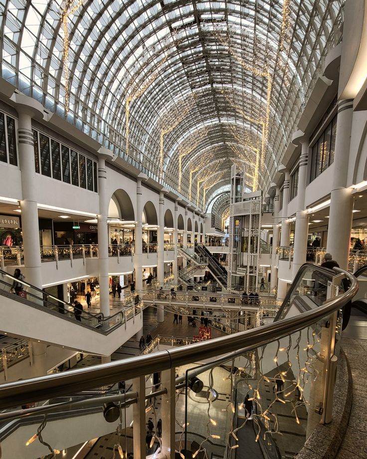 the inside of a shopping mall with people walking around and on escalators in it