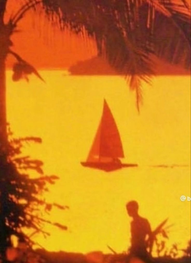 a red sailboat is in the water near some palm trees and a man on a surfboard