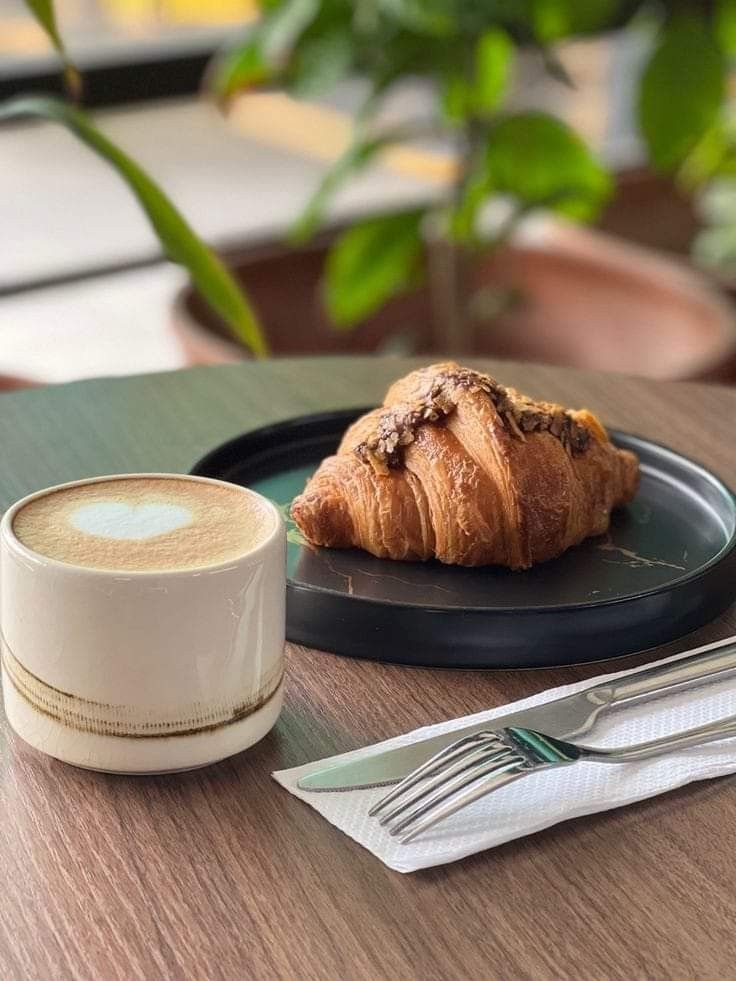 a croissant on a plate next to a cup of coffee