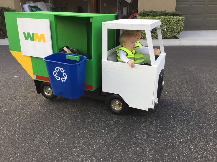 a young boy riding in the back of a green and white truck with a garbage can