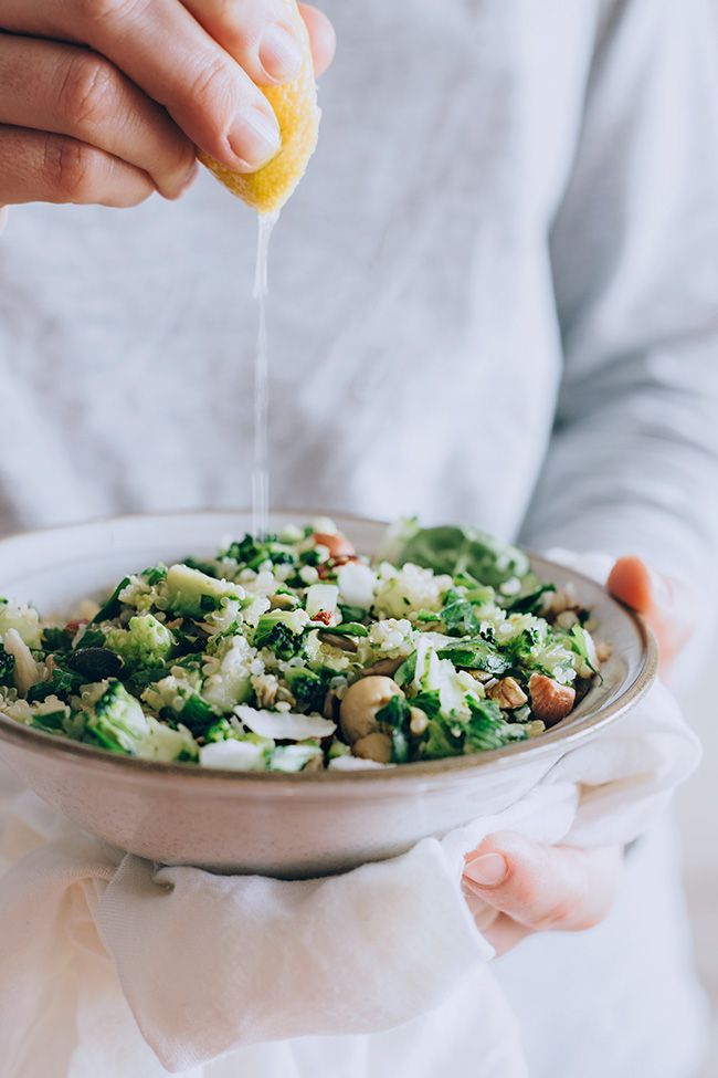 a person holding a bowl filled with vegetables and dressing being drizzled over it