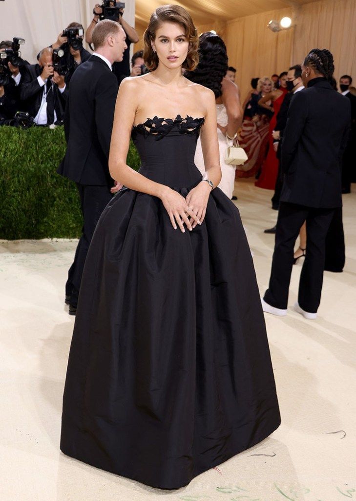 a woman in a black strapless dress standing on a white carpet with cameras around her