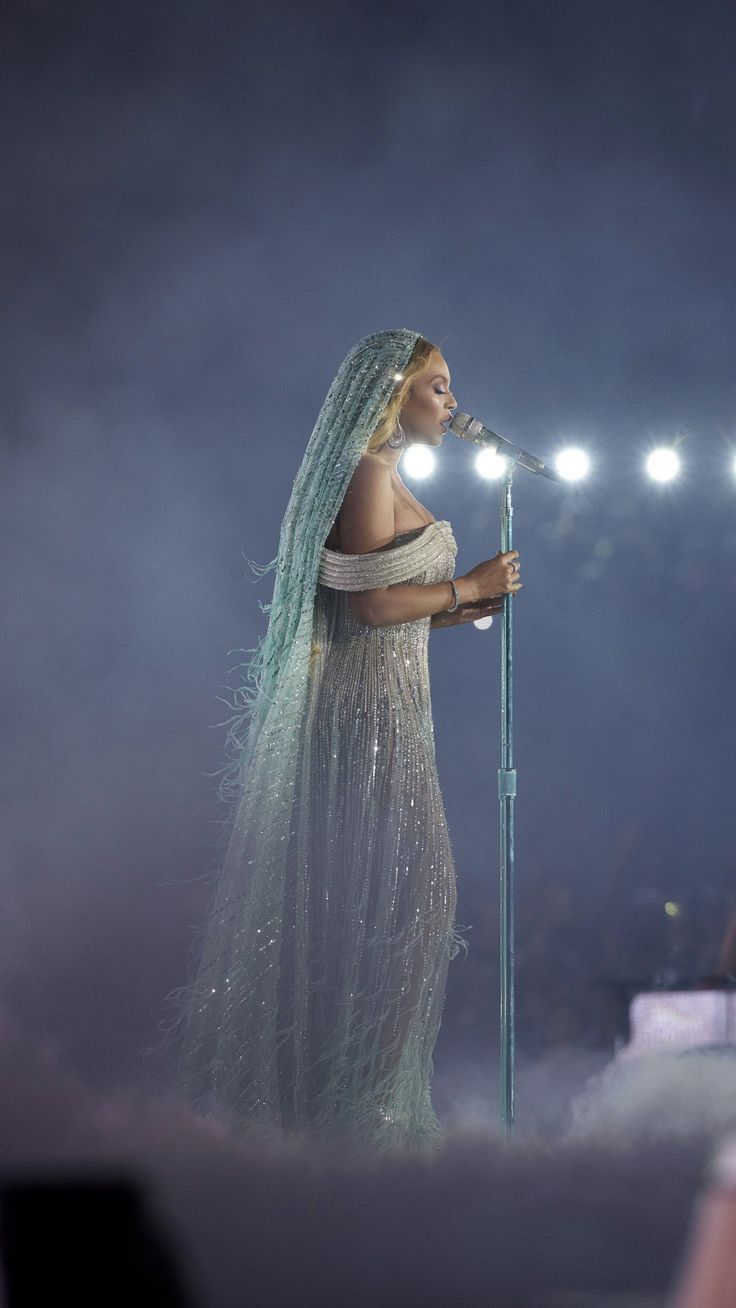 a woman in a white dress holding a microphone and singing into a microphone at a concert